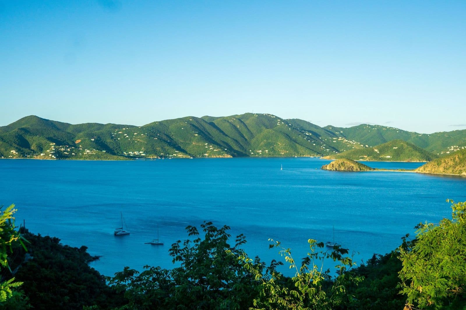Sailboats on blue water below green hills in the British Virgin Islands