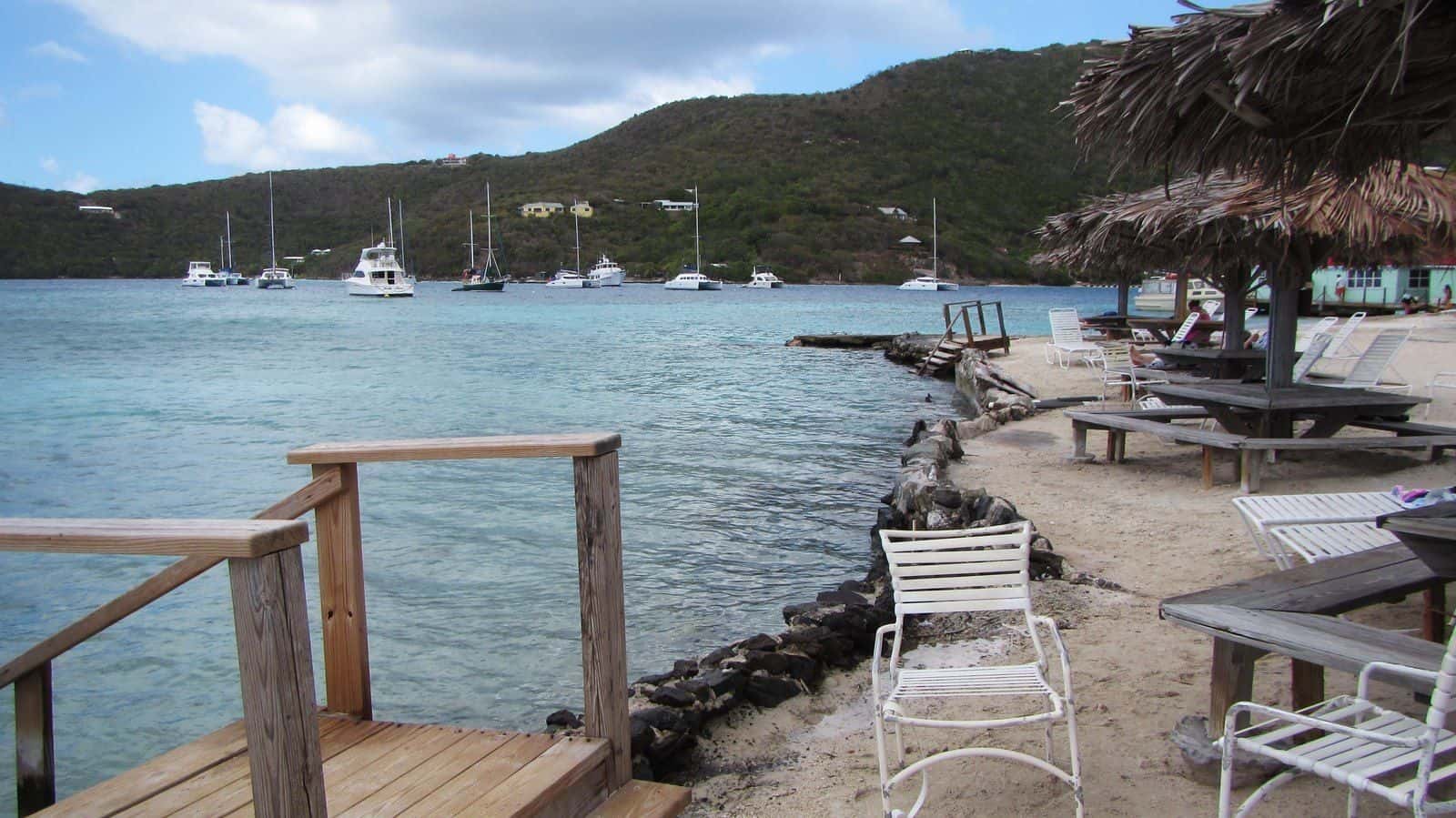 Thatched umbrellas, tables and a deck at the Marina Cay beach bar, boats moored beyond