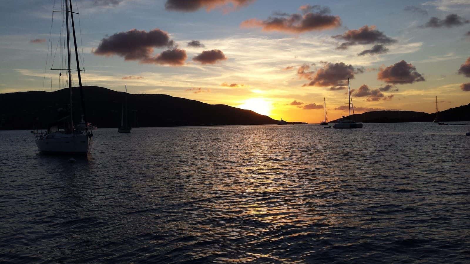 Sailboats at anchor in a British Virgin Islands bay at sunset, the sun setting behind a low island