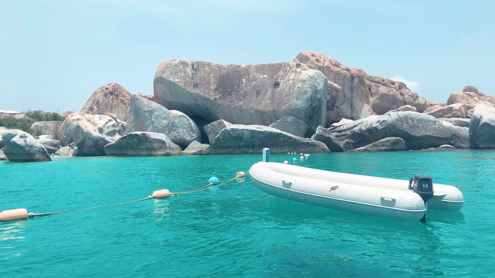 The Baths, Virgin Gorda, from the water: granite boulders above turquoise water, a dinghy moored