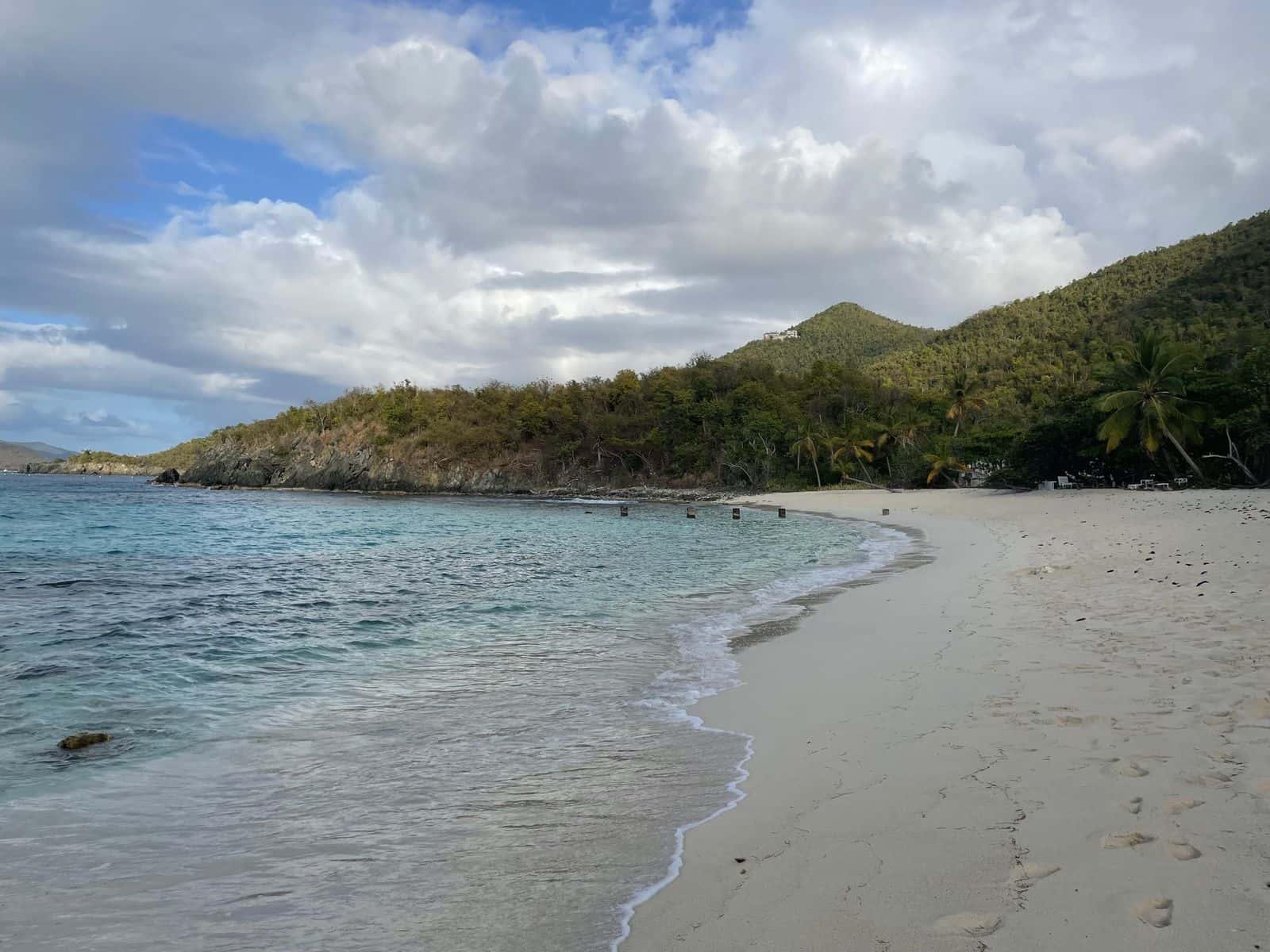 The curve of white sand at Denis Bay, St. John, looking east along the waterline, with palms and a green hillside behind.