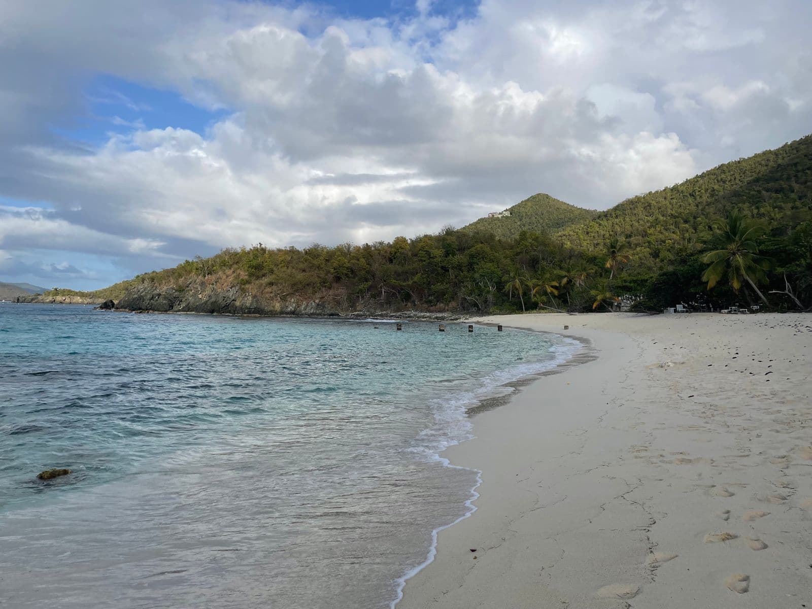 The curve of white sand at Denis Bay, St. John, looking east along the waterline, with palms and a green hillside behind.