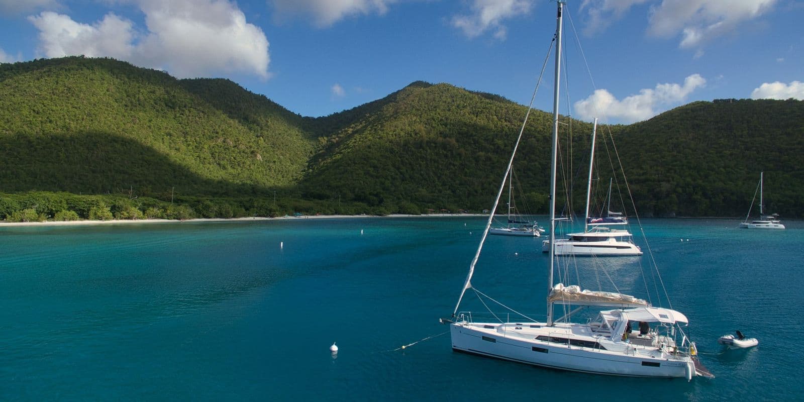 A sailboat on a mooring in calm blue water under green hills, St. John.
