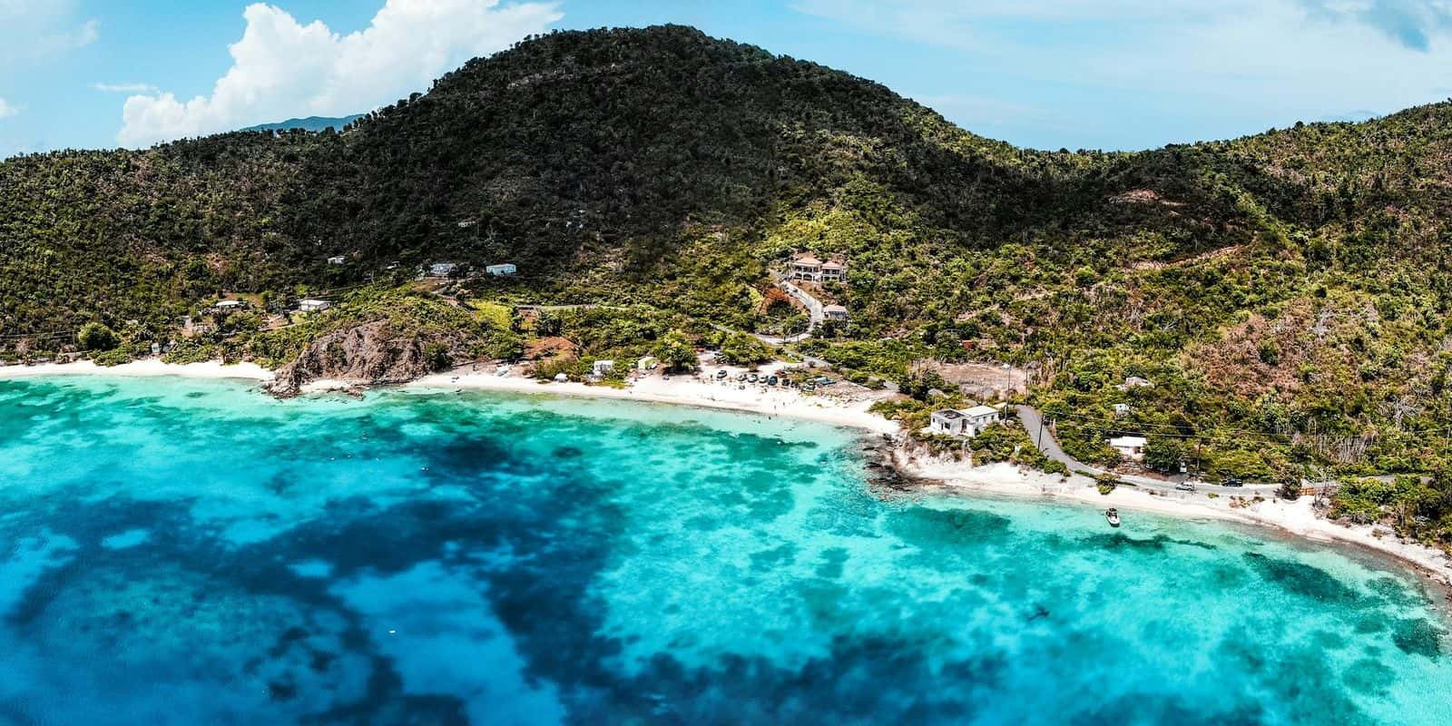 Aerial view of Hansen Bay on St. John's East End: a white beach under a green hill, reef and turquoise water.