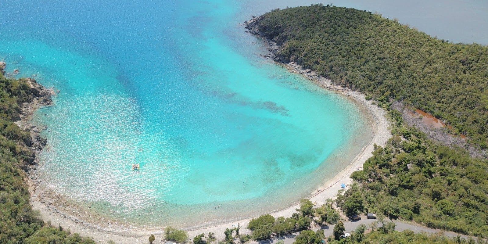 Aerial view of Haulover Bay on St. John's East End: a curve of pale beach, the road behind it and turquoise shallows.