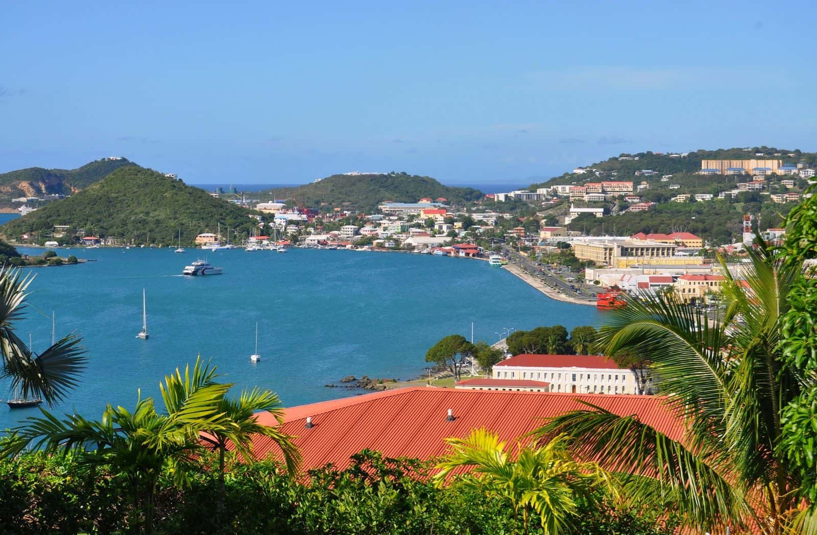 Charlotte Amalie harbor, St. Thomas, framed by palms and a red roof, with boats at anchor and the town on the hillside.