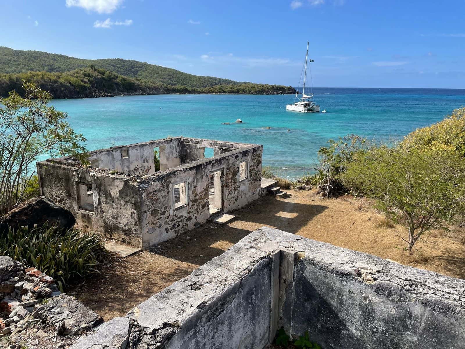 A roofless stone ruin on a rise above Lameshur Bay, St. John, with a catamaran at anchor in the water behind it.