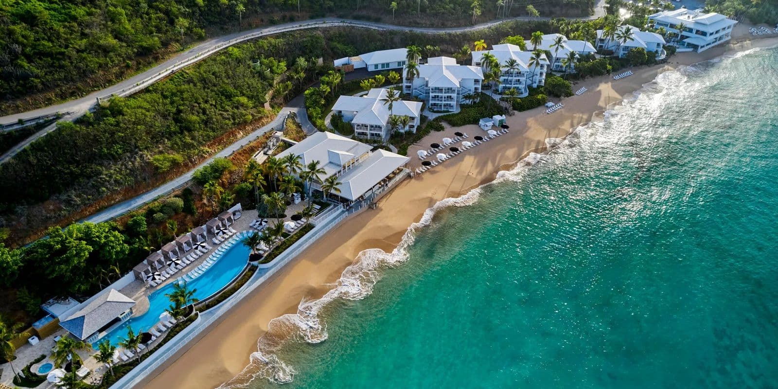 Aerial view of Morningstar Beach, St. Thomas: surf running onto the sand below resort buildings and a pool.