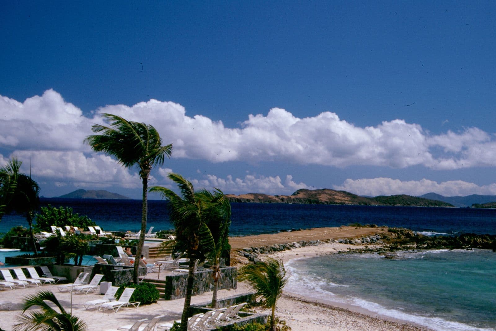 The east end of Sapphire Beach, St. Thomas, from above, with a pool deck, palms, the rocky point and cays beyond.