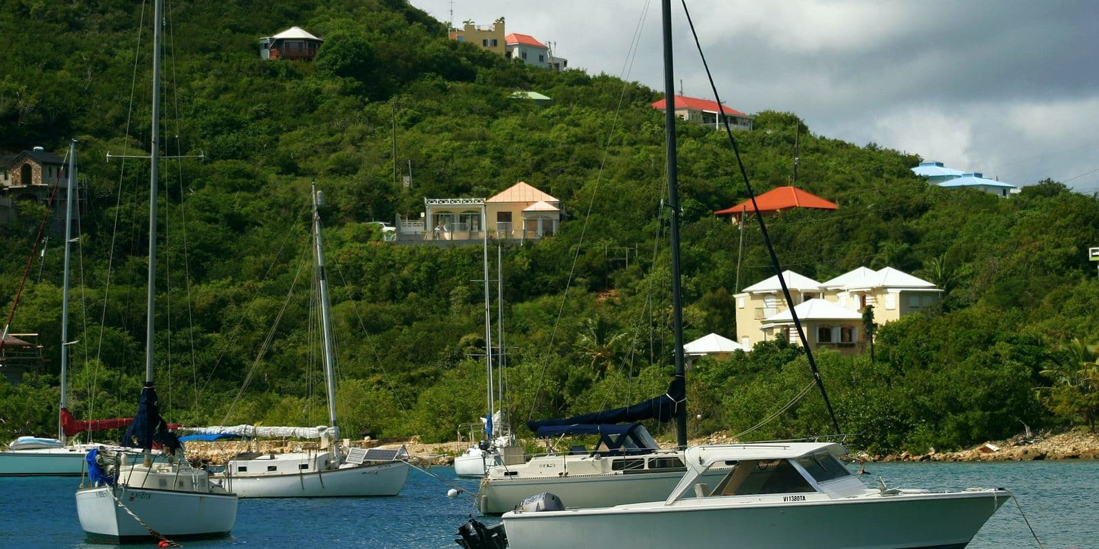 Sailboats and a motorboat at anchor below a green hillside with houses, U.S. Virgin Islands.