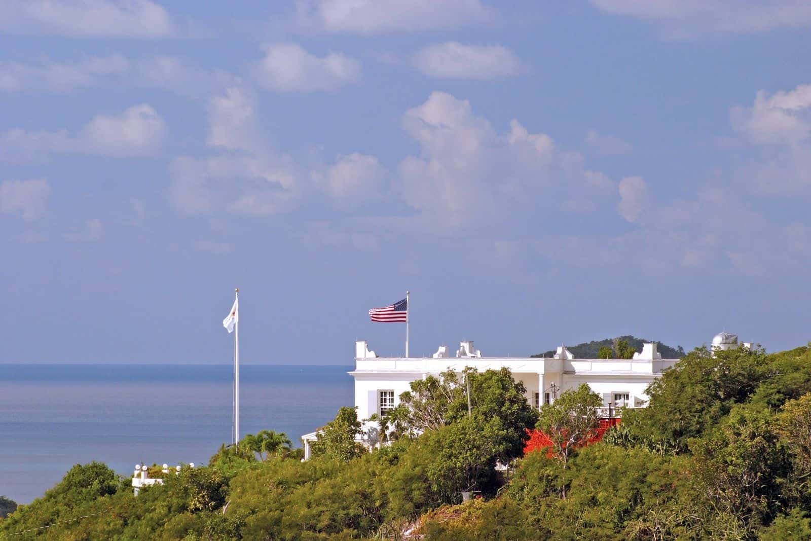 The US Virgin Islands flag, white with a yellow eagle, flying beside the US flag on a hilltop